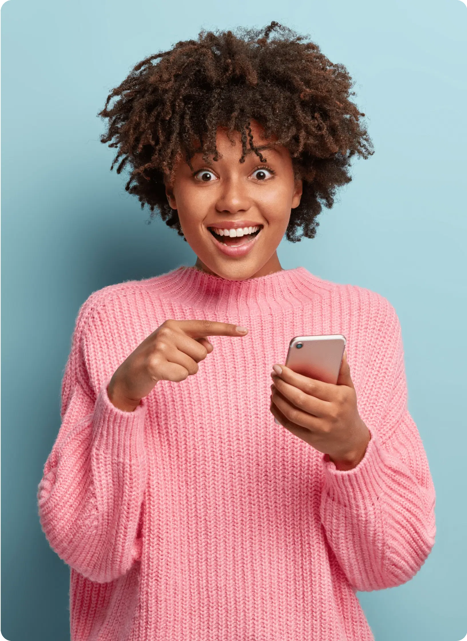 Excited young woman in a pink sweater holding and pointing at her smartphone.